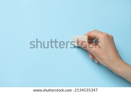 Woman erasing something on light blue background, closeup. Space for text