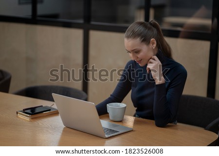 woman of european appearance strong confident young pretty brown-haired woman is working types on the computer. looks into a laptop and smiles. office setting