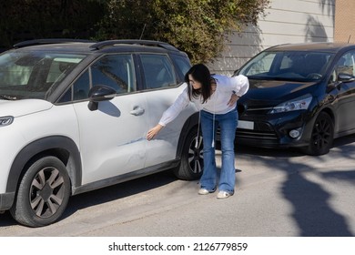 Woman evaluating the damage in her car, done while it was parked in the street. She is calm because has a good car insurance, and she knows that the company will take care of the situation. - Shutterstock ID 2126779859