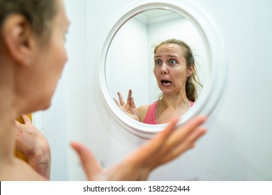 Woman Examines Acne In The Bathroom Mirror. The Girl Is Frightened By Her Appearance, Hatching In The Mirror. Bad Skin