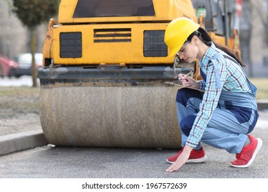 Woman examines asphalt pavement in front of asphalt paver