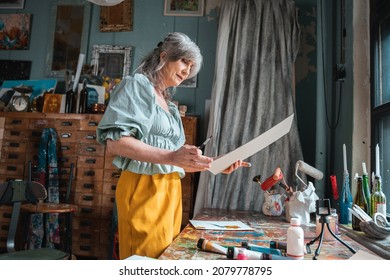 Woman examining her artwork while standing at the workroom around her equipment - Shutterstock ID 2079778795
