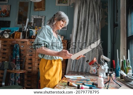 Woman examining her artwork while standing at the workroom around her equipment