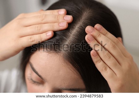 Woman examining her hair and scalp on blurred background, closeup
