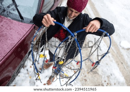 Woman Examining Tire Chains, Confused Yet Determined to Tackle Unfriendly Winter Weather and Learn the Art of Installation in the Midst of Snowfall