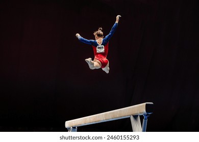 woman exercise on balance beam gymnastics, perform split jump on black background