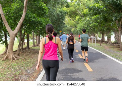 Woman Exercise Walking In The Park With Group People In Blur Background.