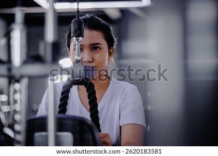 A woman exercises using a cable machine at the gym, her focus is palpable as she works toward her fitness goals with unwavering concentration and determination to build muscle.