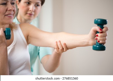 Woman exercising with dumbbells insured by physiotherapist