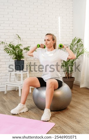 Woman exercising with dumbbells on a stability ball in a indoor space