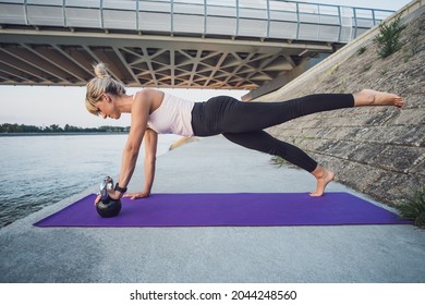 Woman Exercising Kettlebell Pilates Outdoor. Plank With Leg Lift Exercise.