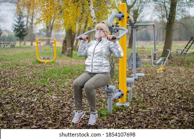 Woman Exercising On A High Pull Chair And Wearing Protective Face Mask, Open Gym