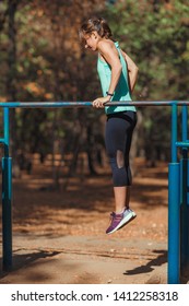 Woman Exercising On Parallel Bar In The Park With Personal Trainer