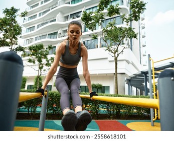 Woman exercising on parallel bars in an outdoor gym environment surrounded by greenery and modern architecture - Powered by Shutterstock