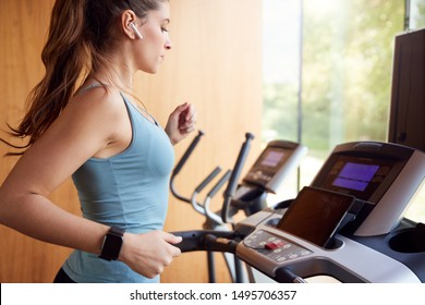 Woman Exercising On Treadmill At Home Wearing Wireless Earphones Checking Smart Watch - Powered by Shutterstock