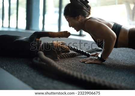 
Woman exercising while her dog lies nearby, woman doing plank teasing and playing with pet at fitness gym
