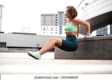 Woman exercising working out triceps and biceps doing dips on urban street in morning