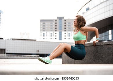 Woman exercising working out triceps and biceps doing dips on urban street in morning