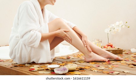 Woman Exfoliating And Moisturizing Her Legs By The Bathtub.