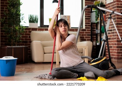 Woman Exhausted After Spending All Day Cleaning And Tidying Apartment, Sitting Taking A Break Holding The Mop. Housewife Feeling Fatigue After Finishing Spring Cleaning At Home.