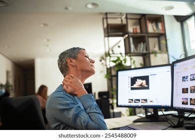 Woman experiencing neck pain while working at desk with dual monitors in office