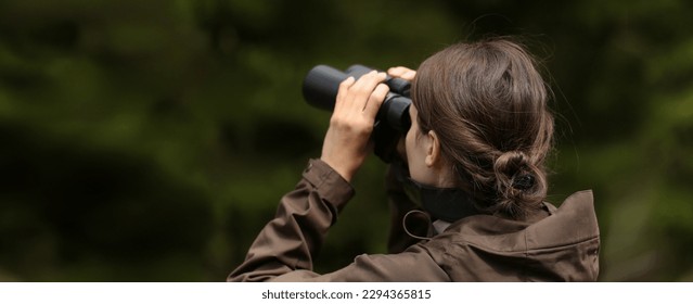 Woman explorer with binoculars showing with finger for animal in the wild forest. Blur dark background. The concept of hunting, travel and outdoor recreation. female hunter with binoculars - Powered by Shutterstock