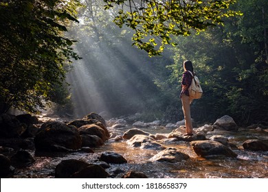 A woman explores new, magical, and fantastic places around the world, surrounded by nature and spreading her arms to breathe and relax. Female hiker crossing the forest creek. - Shutterstock ID 1818658379