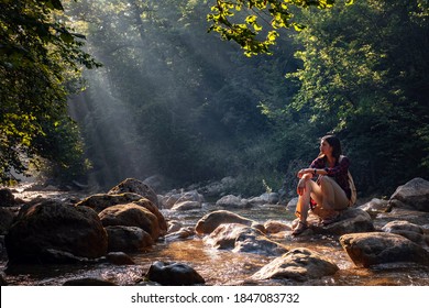 A woman explores new, magical, and fantastic places around the world, surrounded by nature and spreading her arms to breathe and relax. Female hiker crossing the forest creek. - Powered by Shutterstock