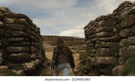 A woman explores a stone passage between two ancient walls at Castro de Baroña, an iconic Iron Age fortification in Porto do Son. The scene captures both history and adventure in a natural landscape - Powered by Shutterstock