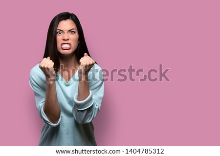 Woman with extreme rage, clinched fists and jaw, angry, emotional, and furious, isolated on pink background, copy space