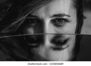 Woman eyes closeup reflected in mirror. Hypnotize strong look. Hypnotic deeply penetrating glance. Revengeful insidious expectant gaze. Young caucasian girl face. Black and white portrait. Good vision