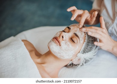 Woman face getting facial care with cream by beautician hands at spa salon. Close-up portrait. - Shutterstock ID 2110072157