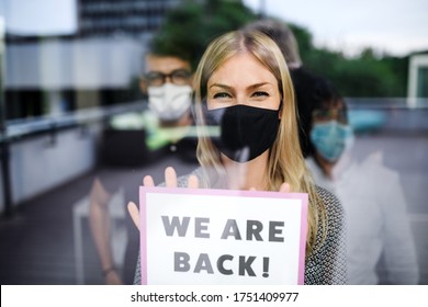 Woman With Face Mask Back At Work In Office After Lockdown, Holding We Are Back Sign.