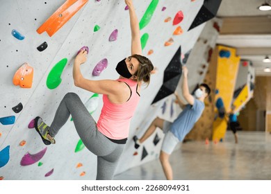 Woman in face mask climbing on rock-climbing wall during training in bouldering gym. - Powered by Shutterstock