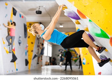 Woman in face mask climbing on rock-climbing wall during training in bouldering gym. - Powered by Shutterstock