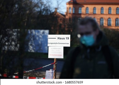 Woman With Face Mask In Front Of Information Sign, Translation: Building 19, Clarification Center Coronavirus, Hours: 10-19, Weekends 10-17, Please Use Wayfinding System                               