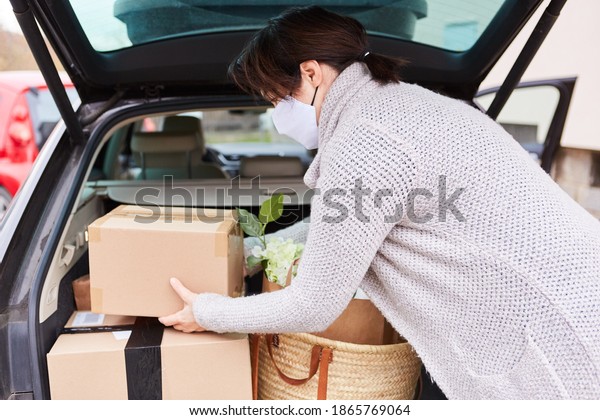 Woman with face mask loads full car trunk with\
packages and purchases