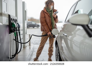 Woman in face mask refueling car with a gasoline, using smartphone to pay. Concept of mobile technology for fast refueling without visiting the store - Powered by Shutterstock