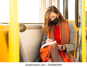 A Woman Face Mask Writes In A Diary While Riding The Public Bus To Work. 