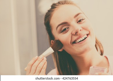 Woman face painting. Girl applying rouge or bronzing powder with brush to her skin in bathroom. Makeup cosmetics and beauty procedures.