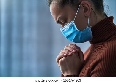 Woman In Face Protective Mask With Closed Eyes And Praying Hands, Asks God For Healing And Recovery During Cancer Sickness, Health Problems And Covid Coronavirus Epidemic. Copy Space 