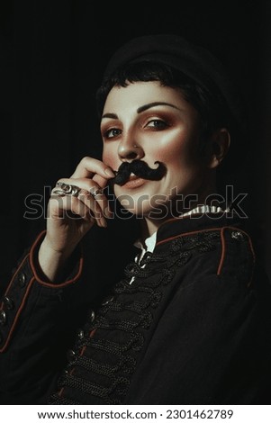 A woman with a fake moustache and a black jacket is posing for a photo as a hussar
