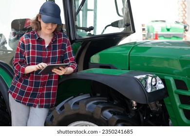 Woman farmer with a digital tablet on the background of an agricultural tractor. - Powered by Shutterstock