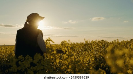 A woman farmer stands in a rapeseed field at sunset. Beautiful rural landscape. - Powered by Shutterstock