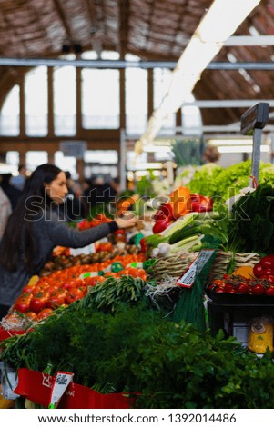 Woman at a farmers market selecting fresh seasonal produce, with peppers, tomatoes, herbs and spices, leaks, cucumbers, onions in the shot