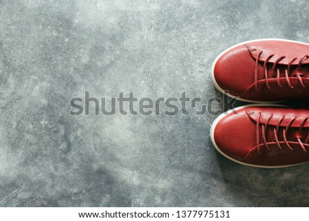 Woman fashion terracotta color shoes on gray stone background. Top view on red sneakers with copy space.