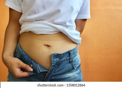 Woman Fat Problem, Person In White Shirt With Blue Jeans Try To Put Button On Pants And Shows Belly, Orange Background