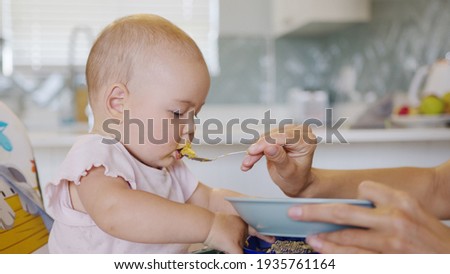 Woman feeding child with spoon. Mom feed baby with pureed food. Mom feeding kid in baby chair.