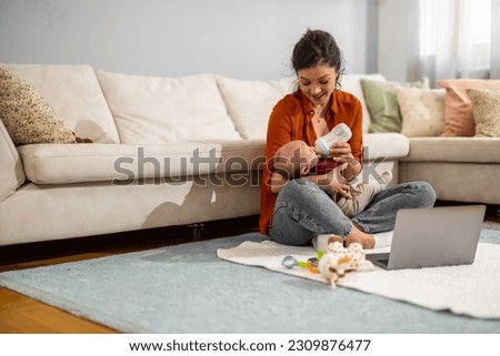 Woman feeding newborn with milk in a bottle.Beautiful mom feeds baby with formula while sitting on floor at home.