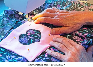 A Woman Feeds Two Pieces Of Brightly Colored Fabric Together As She Feeds Them Through Her Sewing Machine.